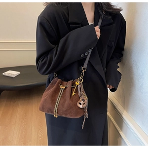 Close-up of vintage brown suede bucket bag with gold chain drawstring and charms