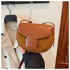 Detailed view of brown saddle bag with white contrast stitching and mixed textures