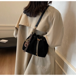 Detail of vintage matte black bucket bag with gold chain drawstring on a trench coat
