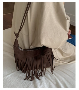 Detail of dark brown suede crossbody bag featuring dense fringe and slim knotted strap