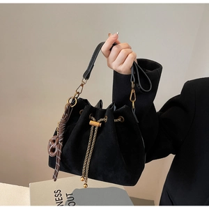 Detail of black drawstring bucket bag with gold chain hardware and woven charm accessory