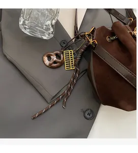 Detail of matte brown bucket bag with pretzel charm and golden abacus pendant