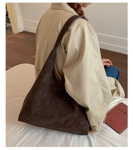 Close-up of a dark brown suede tote bag worn on shoulder in a minimalist indoor setting