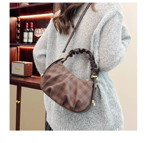 Detail of dark brown checkered crossbody bag with ruched handle on a female model