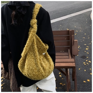 Close-up of mustard yellow plush knit shoulder bag with knotted strap on street background