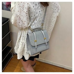 Détail d'un sac bandoulière gris Morandi avec ferrures dorées porté par un mannequin de dos