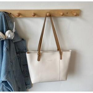 Détail du sac fourre-tout crème avec bandoulières marron sur un support en bois