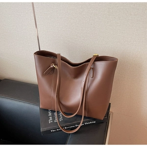 Détail d'un sac cabas en cuir marron avec lettrage doré posé sur un livre pour le travail