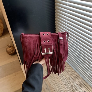 Sac bandoulière rétro en daim bordeaux avec franges et boucle sur fond de décor en bois