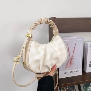 Cream plaid crescent shoulder bag with pleated handle and golden hardware on books