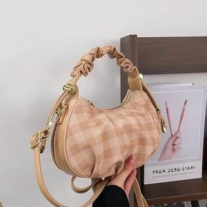 Beige plaid crossbody bag with ruched top handle and adjustable strap in modern setting