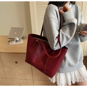 Détail du sac cabas en cuir bordeaux avec coutures verticales et logo embossé élégant