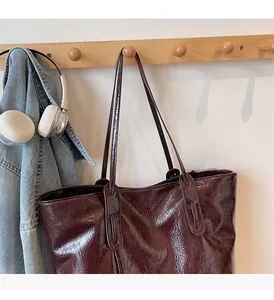 Detail of deep brown tote bag with wrinkled leather texture hanging on a wooden rack