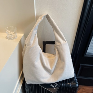 Gros plan du sac hobo en velours côtelé beige posé sur une valise en décor de voyage