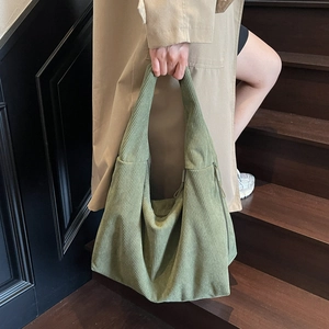 Détail du sac cabas en velours côtelé vert herbe tenu par un mannequin sur un escalier