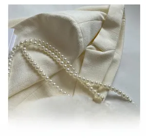 Detailed close-up of glossy pearl shoulder strap on elegant cream tweed fabric