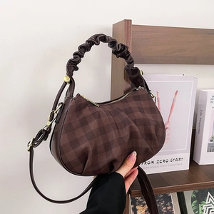 Brown plaid crossbody bag with pleated handle and golden hardware on a wooden shelf