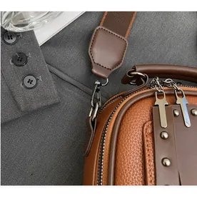 Macro detail of brown lychee leather handbag with wide canvas strap and metal hook