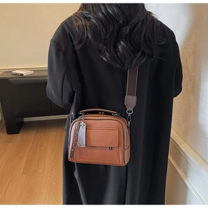 Detail of a brown leather crossbody bag with wide strap and pebble grain texture