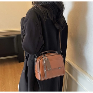 Close-up of brown textured leather crossbody bag with dual zippers and rivet details