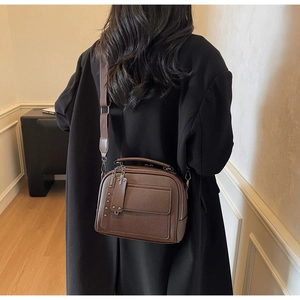 Detail of dark brown pebble leather crossbody bag with wide strap on a black wool coat