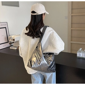 Sac hobo matelassé argenté avec bandoulière large porté par un mannequin en extérieur