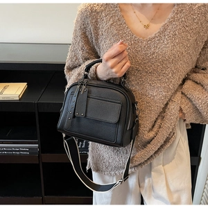 Close-up of black litchi grain leather bag with wide woven strap and metal rivets