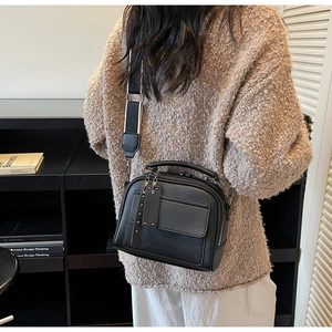 Detail of black pebbled leather crossbody bag with wide black and white shoulder strap