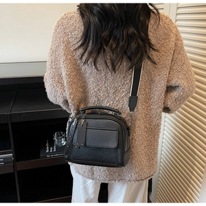 Detail of black lychee leather crossbody bag with wide striped strap and rivet accents
