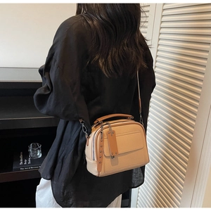 Detail view of beige crossbody bag with textured leather and brown tassel detail on model