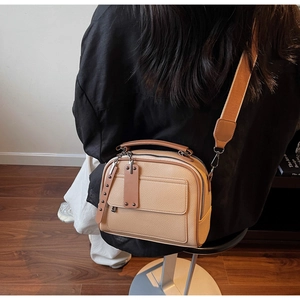 Detail of cream crossbody bag with wide strap and brown trim worn in lifestyle setting