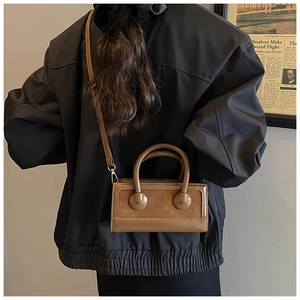 Detail of a brown rectangular crossbody bag with dual-texture finish on a black jacket