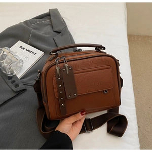 Detail of brown lychee grain leather handbag with wide strap and multi-zipper layers