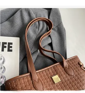 Detail of woven brown tote bag featuring smooth leather handles and gold metal buckles