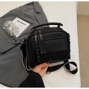 Detail of black lychee grain leather crossbody bag with metal rivets and wide strap