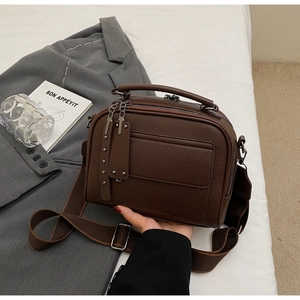 Detail of dark brown lychee leather crossbody bag with triple zipper layers and wide strap