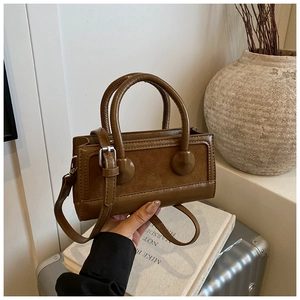 Detailed shot of brown mixed leather shoulder bag with dual handles and silver buckles
