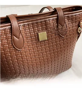 Macro view of woven leather texture with gold square metal hardware on brown tote bag