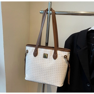 Detail of woven beige leather tote bag with brown handles and golden hardware