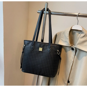 Detail view of black woven tote bag with gold metal plaque on a neutral background