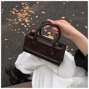Close-up of deep brown glossy patent leather handbag with dual handles in autumn setting