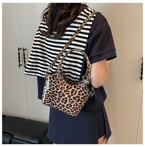 Detail of glossy leopard print handbag featuring polished silver buckles and a long strap