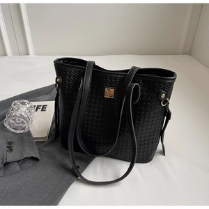 Detailed view of black woven tote bag featuring metallic gold square plate and sleek straps