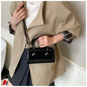 Polished black patent leather mini bag with circular handles on model in suit