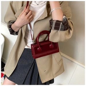 Detail of dark red glossy mini crossbody bag styled with a khaki trench coat