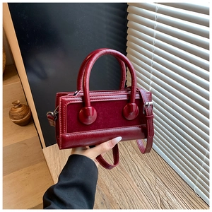 Detail of burgundy rectangular handbag with mixed leather texture and sphere buckle accents