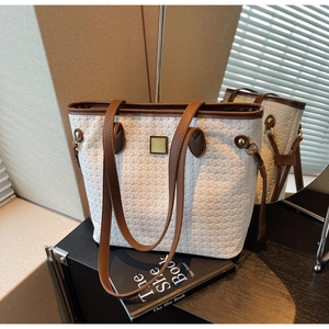 Detailed close-up of woven tote bag with brown leather strap and golden buckle accent