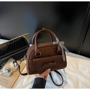 Detail of dark brown suede shoulder bag with ribbon charm and sleek leather handle