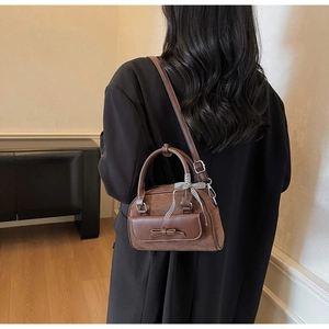 Détail du sac à main en cuir marron avec nœud à carreaux et finition en daim mélangé
