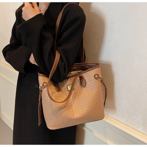 Detail of a brown woven tote bag with leather straps on a model wearing a black coat